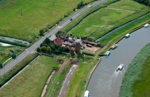 Ariel view of the windmill and buildings that make up the Stracey Arms Windpump, Tunstall. Green fields surround the buildings and pleasure boats travel along the wide stretch of water which runs past the location.