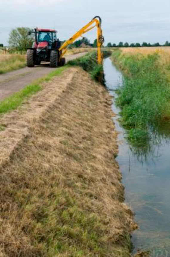 A tractor travels along a drainside road using its outreached hydraulic arm to carry out routine weed cutting and flailing of the drain’s bank sides