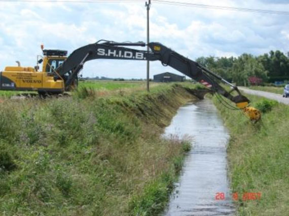 A tracked excavator uses its long-reach hydraulic arm to carry out routine weed cutting and flailing of the drain’s bank sides