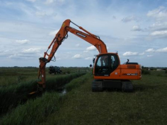 A tracked excavator uses its outreached hydraulic arm to carry out routine weed cutting and flailing of the drain’s bank sides